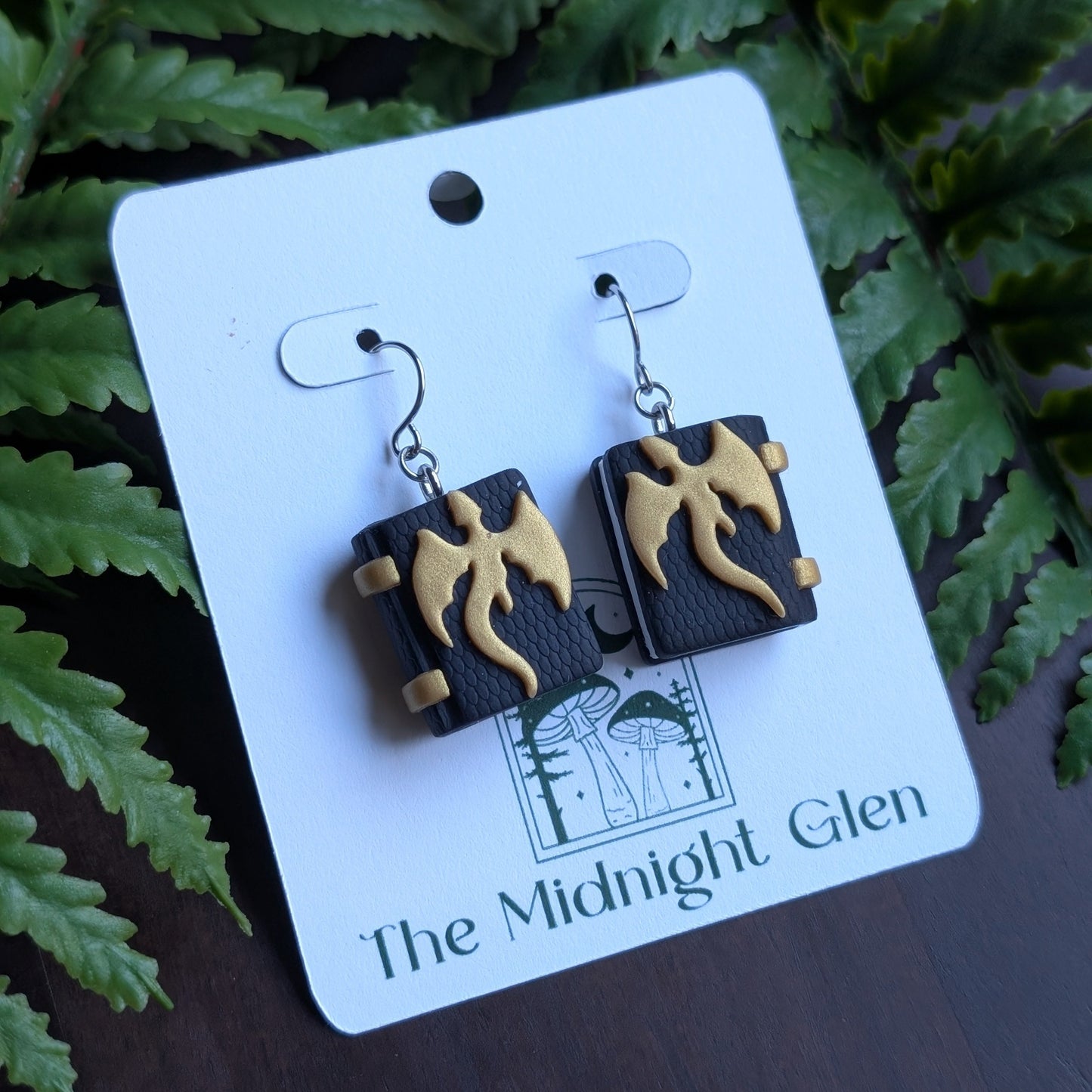 Pair of earrings on a card with 'The Midnight Glen' branding against a fern background