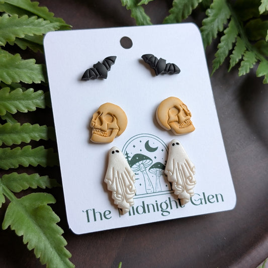 Set of Halloween-themed earrings on a card with 'The Midnight Glen' branding, surrounded by green leaves.